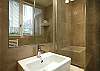 In the bathroom, you have an extra large mirror and lights and an extra large modern shower with a glass door.