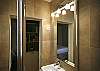 In the bathroom, you have an extra large mirror and lights and an extra large modern shower with a glass door.
