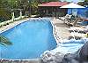 Large pool with waterfall, next to the bar with BBQ grill, as well as a wall mural painted, lounge chairs and garden table at Villa Jaco Sol vacation rental in Jaco, Costa Rica.