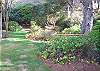 Large grassy backyard with small bridge that goes across a little stream.