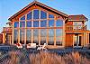 View of house from the beach with large deck patio with built in firepit and patio furniture.