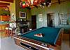 This family/living room has a pool table, kitchen and doors leading outside.