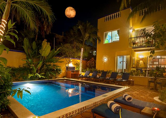 Evening view of the tropical pool area with lounge chairs, warm lighting, and lush gardens—perfect for a relaxing dip after the beach.