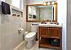 Bathroom inside Abbey del Sol A2 Unit 10, a Puerto Morelos vacation rental, featuring a wood vanity, large mirror, toilet, tiled walls, and a clean, practical shower area.