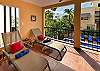 Private balcony at Abbey del Sol A2 Unit 10, a Puerto Morelos vacation rental, featuring lounge chairs, colorful cushions, shade, tropical plants, and a view over the pool and courtyard.