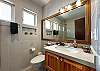 Bathroom inside Abbey del Sol A2 Unit 10, a Puerto Morelos vacation rental, featuring a wood vanity, large mirror, toilet, tiled walls, and a clean, practical shower area.