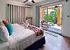 Bedroom inside Abbey del Sol A2 Unit 10, a Puerto Morelos vacation rental, featuring a king bed, colorful accents, air conditioning, natural light, and balcony doors leading to a private outdoor seating area.
