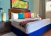 Bedroom detail inside Abbey del Sol A2 Unit 10, a Puerto Morelos vacation rental, featuring a king bed, colorful pillows, towel art, bedside lamps, and tropical wall art for a bright and welcoming stay.