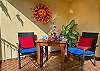 Private balcony corner at Abbey del Sol A2 Unit 10, a Puerto Morelos vacation rental, featuring two chairs with colorful cushions, a small table, tropical plants, and warm decorative wall art.
