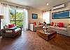 Living room inside Abbey del Sol A2 Unit 10, a Puerto Morelos vacation rental, featuring two sofas, colorful accent pillows, a wooden coffee table, air conditioning, balcony doors, and a comfortable space to relax after a day at the beach.
