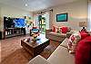 Living room inside Abbey del Sol A2 Unit 10, a Puerto Morelos vacation rental, featuring a sofa with colorful pillows, coffee table, TV, balcony doors, and a relaxed space for unwinding after a day at the beach.