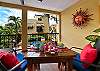Private balcony at Abbey del Sol A2 Unit 10, a Puerto Morelos vacation rental, featuring a table with colorful place settings, red cushions, tropical plants, and a view over the pool and courtyard.