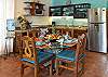 Kitchen and dining area inside Abbey del Sol A2 Unit 10, a Puerto Morelos vacation rental, featuring a dining table with colorful place settings, wood chairs, stainless refrigerator, water dispenser, and a well-equipped kitchen for a comfortable stay.