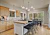 Bright kitchen with island, pendant lighting, wood cabinetry, and tree views.