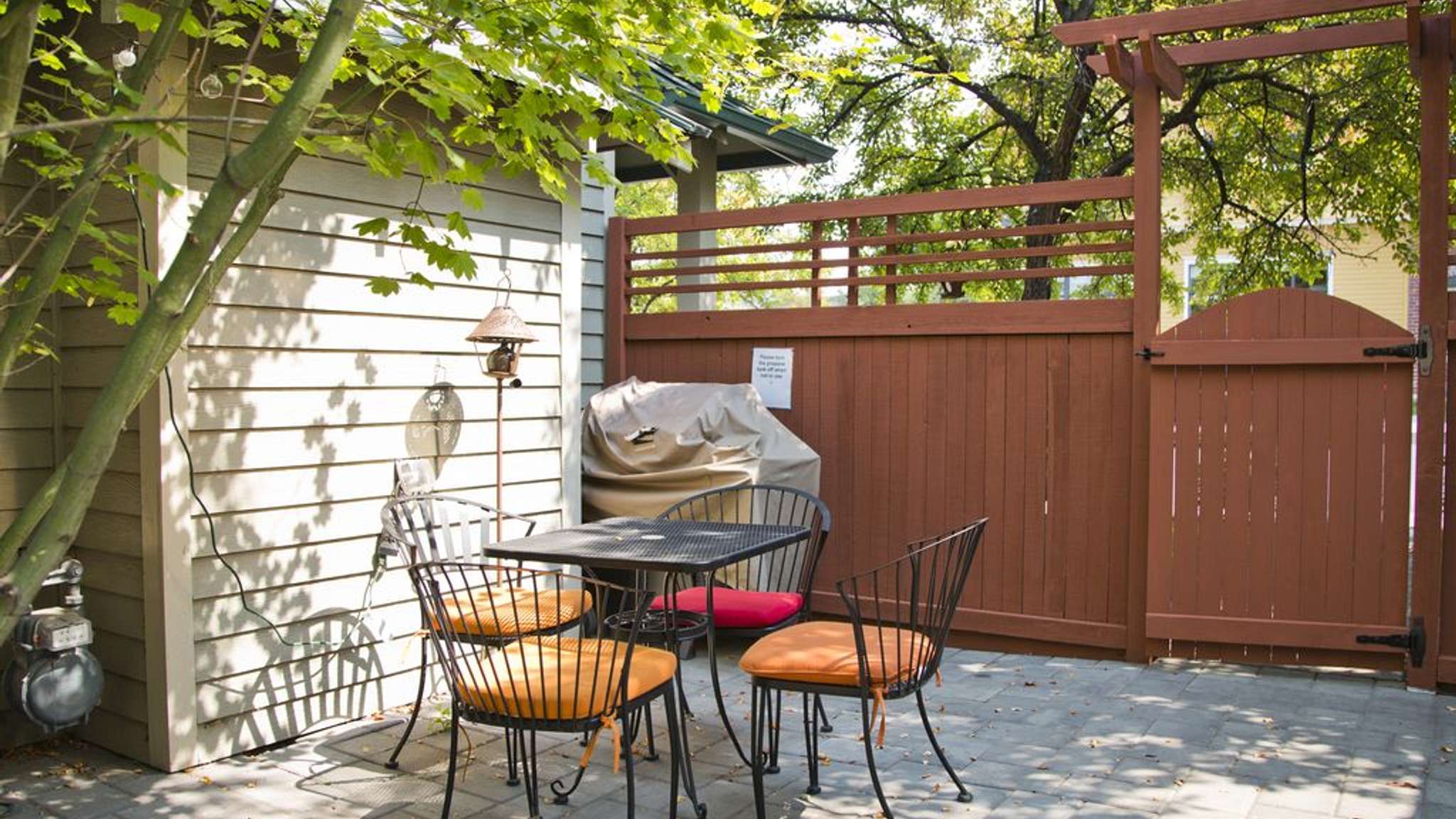 A gas BBQ grill and patio table that seats four is located in a semi-private patio area. 
