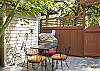 A gas BBQ grill and patio table that seats four is located in a semi-private patio area. 
