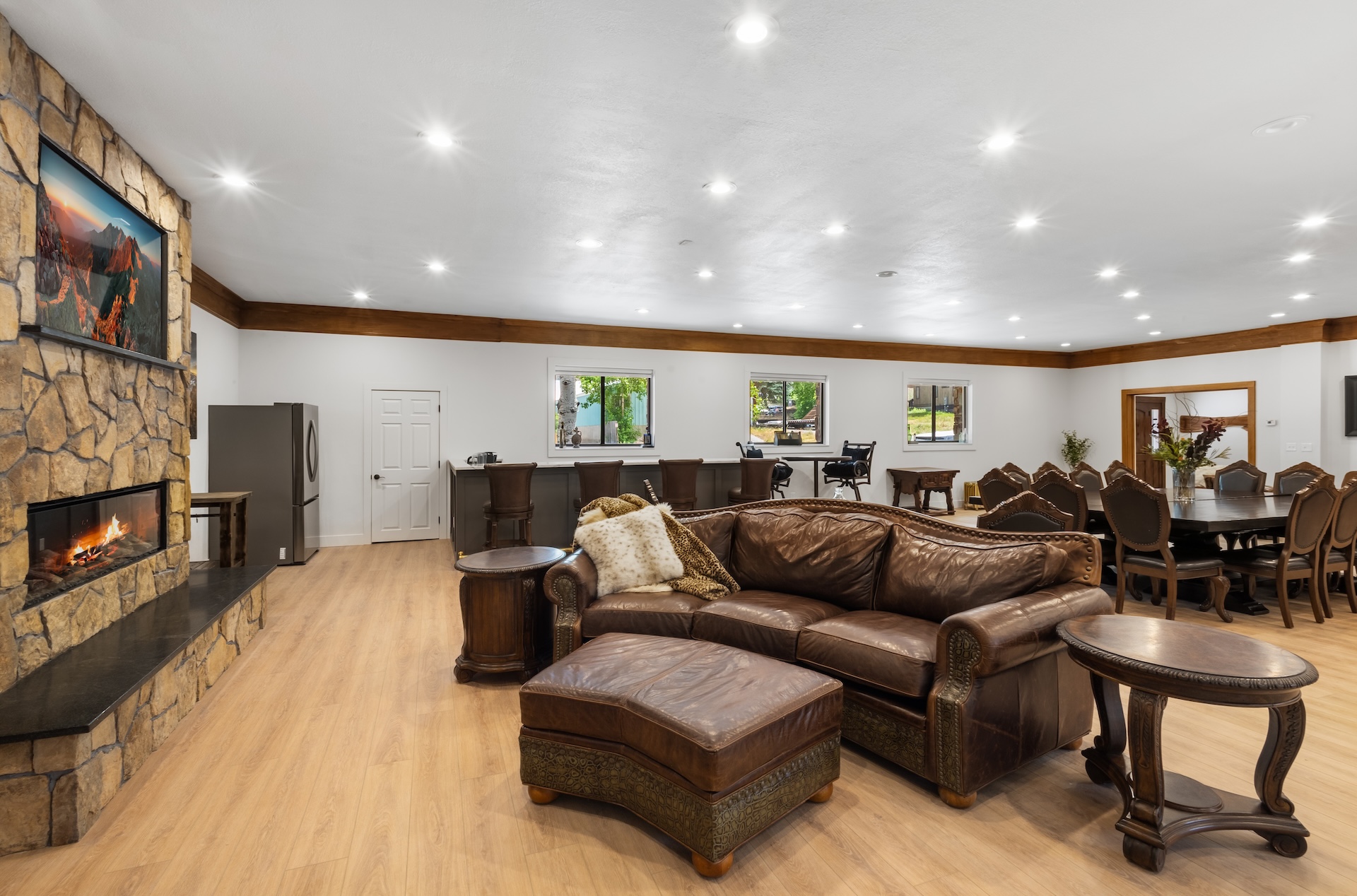 Great room with large fireplace, smart TV, dining space for 14 people, lounging areas, antique piano, and bar. 