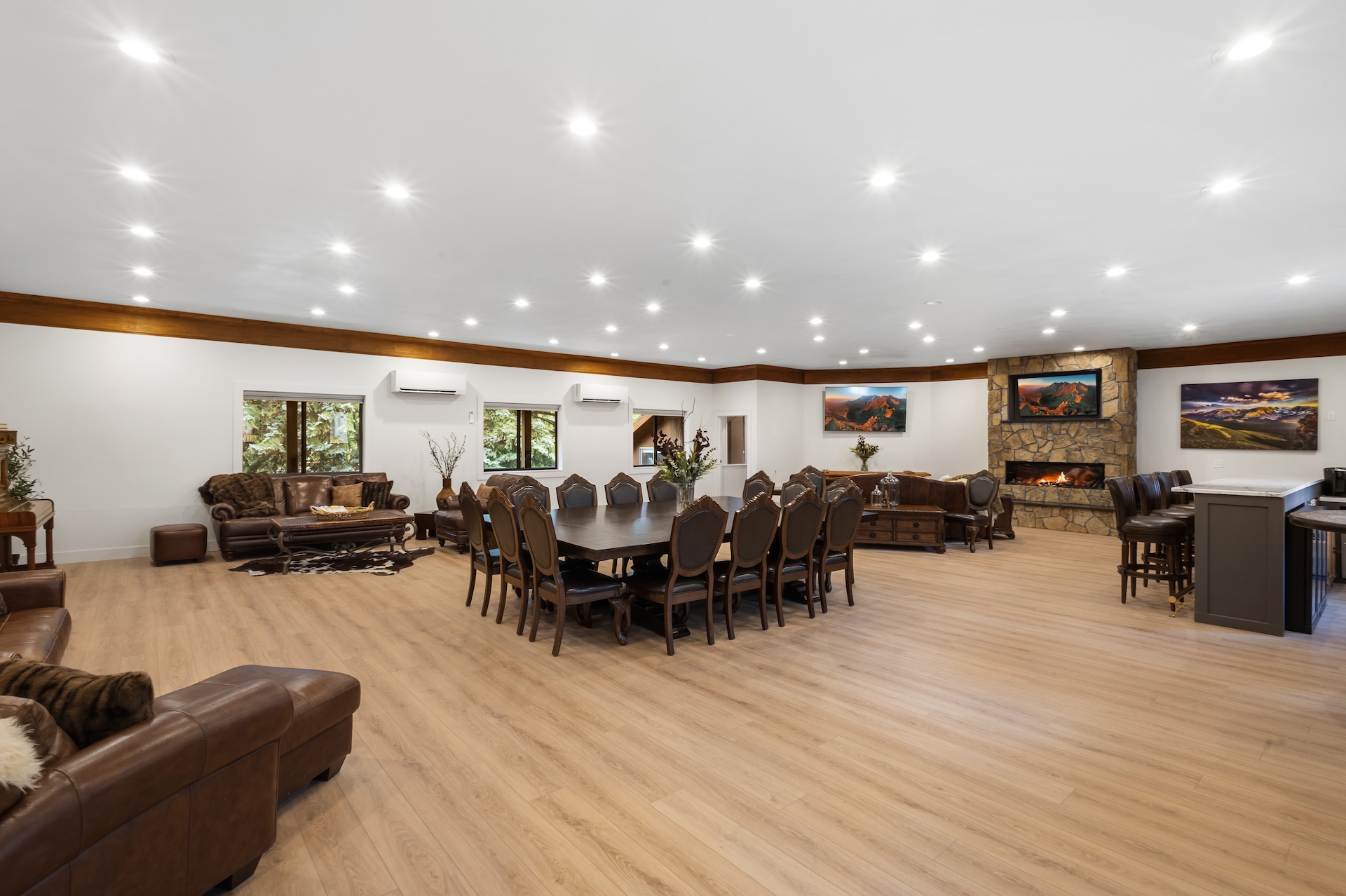 Great room with large fireplace, smart TV, dining space for 14 people, lounging areas, antique piano, and bar. 