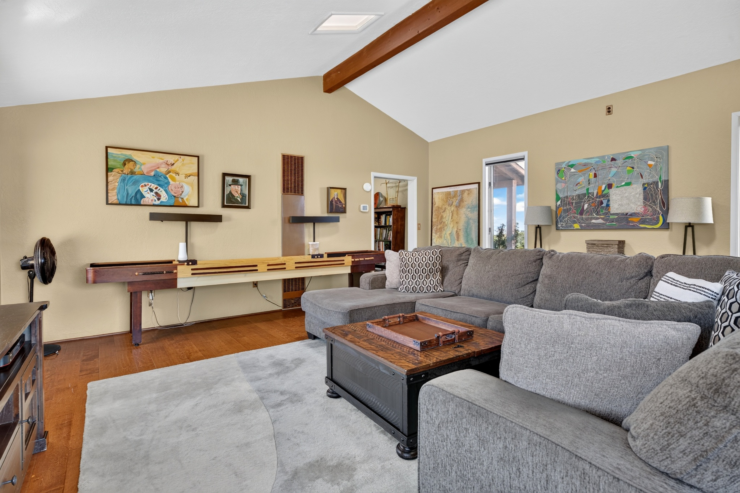 Game room with a regulation shuffleboard table, sectional sofa, smart TV, and a library of movies and games.
