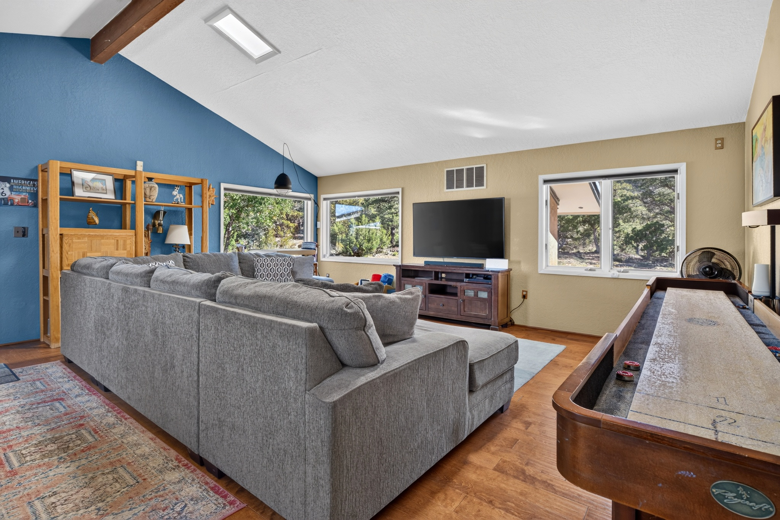 Game room with a regulation shuffleboard table, sectional sofa, smart TV, and a library of movies and games.