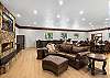 Great room with large fireplace, two Smart TVs, dining space for 14 people, lounging areas, antique piano, pool table, and bar. 