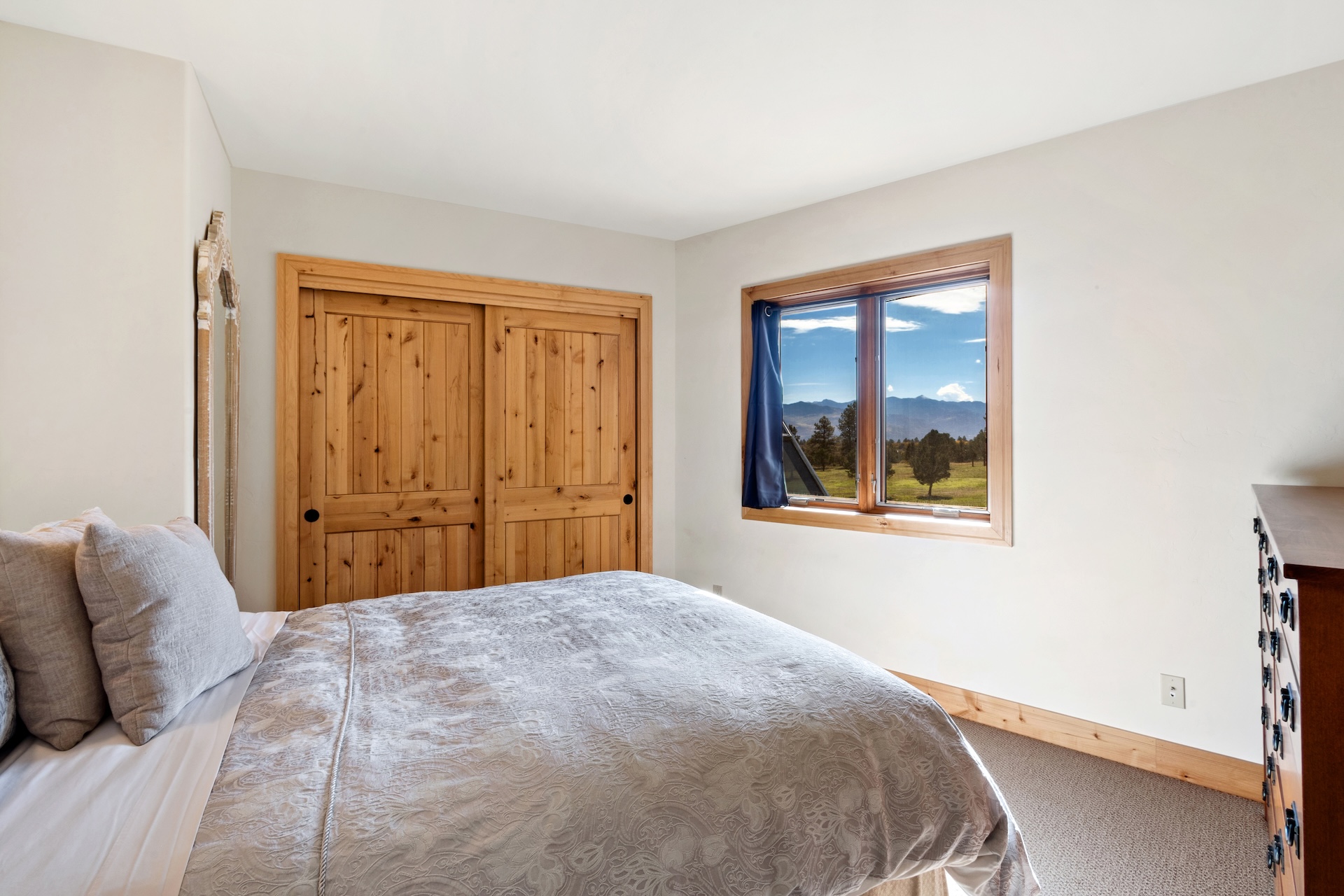 The guest bedroom includes a comfortable queen bed with a large mirror, closet, dresser, and mountain views. 