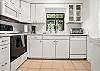 The final kitchen view brings it all together—bright white cabinets, large window over the sink, and everything you need for a laid-back stay. Whether you're making a full dinner or just grabbing plates for takeout, it’s easy, intuitive, and guest-ready.