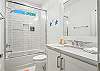 The shared guest bath includes a tiled tub/shower combo, bright vanity, and beachy touches that keep things simple and fresh.