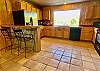 Kitchen #2 has saltillo tile floors, island with bar stools and large picture window overlooking mature trees & distant mountain top.