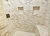 Bunkhouse ensuite bathroom is white stone tile shower, bench, & vaulted ceiling.