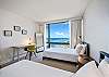 Two twin beds make the guest bedroom flexible for longer stays, while a dedicated desk, individual reading lights, and a full-height window with ocean and marina views support both rest and everyday routines.