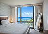 Placed beside a floor-to-ceiling window, the king bed enjoys broad views across Ala Wai Boat Harbor to the Pacific Ocean, while curtains, a bedside light, dresser, and full-length mirror complete the room.