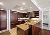 This entry-side view highlights the kitchen’s generous granite work surfaces, dark wood storage, full appliance suite, and open connection to the dining area—useful space for regular home cooking during a monthly stay.