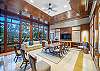 Warm wood finishes, tall windows, lounge seating, tables, and a television define The Watermark Waikiki’s shared clubhouse, a polished community space overlooking the landscaped grounds during a 30+ night stay.