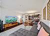 Looking back from the living area, this angle shows how the sectional, television, four-seat dining table, and open kitchen form one connected space for relaxing, dining, and settling into an extended Waikiki stay.