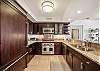 Dark wood cabinetry and granite counters surround the full kitchen, equipped with a refrigerator, stove and oven, microwave, dishwasher, and double-basin sink for the practical demands of a 30+ night stay in Waikiki.