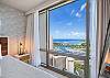 From beside the king bed, the primary bedroom’s floor-to-ceiling window frames Ala Wai Boat Harbor, Magic Island, the Ala Moana coastline, and Pacific Ocean, making the high-floor outlook part of the room’s everyday experience.