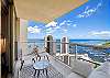 The covered corner lanai/balcony offers multiple cushioned seats and an elevated ocean-and-marina outlook, extending the living space of this two-bedroom condo at The Watermark Waikiki for monthly stays in Honolulu.