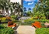 A closer view of the shared garden highlights two benches facing a decorative water feature, with dense palms and colorful landscaping adding depth to The Watermark Waikiki’s private residential grounds in Honolulu.