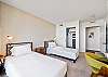 A reverse view of the guest bedroom shows the two twin beds, individual reading lamps, shared nightstand, dedicated desk chair, and closet—practical details for keeping a longer Waikiki stay comfortable and organized.