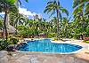 The Watermark Waikiki’s shared heated pool curves through lush tropical landscaping, with palms, rock accents, and a stone-tiled deck creating a resort-style setting within the residential community for 30+ night guests.