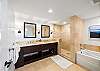 The en-suite primary bathroom provides a double vanity, separate glass-enclosed walk-in shower, bathtub, broad mirrors, and open towel storage—welcome functionality when two guests are sharing a longer stay.