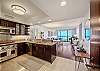 From the entry, the condo opens through a granite-finished kitchen and dining area toward the living room, furnished lanai/balcony, and Pacific Ocean beyond, immediately revealing the home’s open layout for longer Waikiki stays.