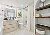 Refresh after a Waikiki beach day in this bright Ilikai bathroom, featuring a tub/shower, generous vanity, open shelving, and calming botanical accents that echo the greenery just outside during your Honolulu stay.