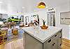 Coastal-style open floor plan view from the kitchen island, showcasing the bright living and dining areas with lush outdoor scenery.