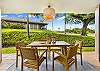 Covered lanai dining area overlooking lush resort landscaping and swaying palm trees.