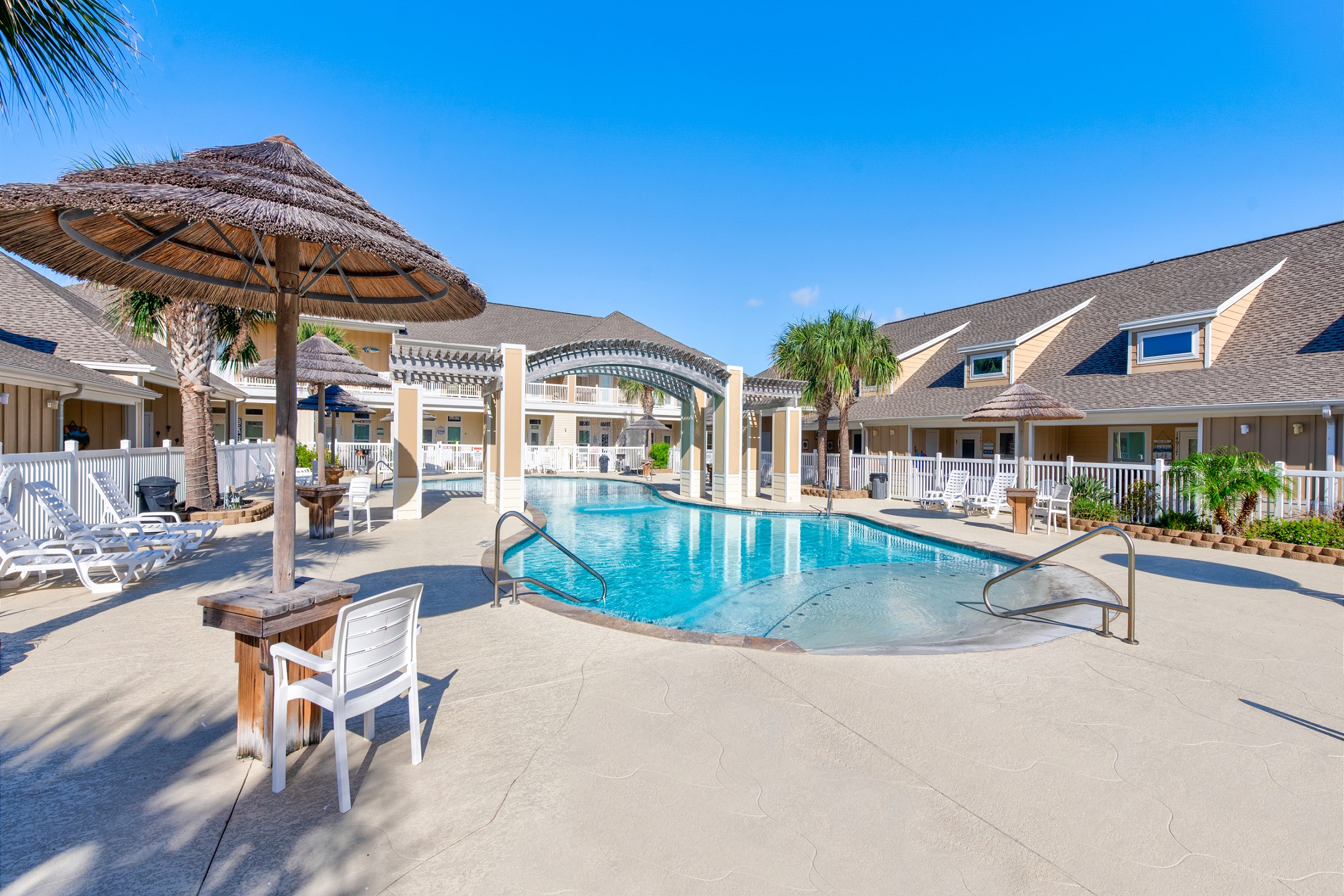 Village by the Beach, heated pool with relaxing chairs, loungers and Tiki huts for those sunshine days