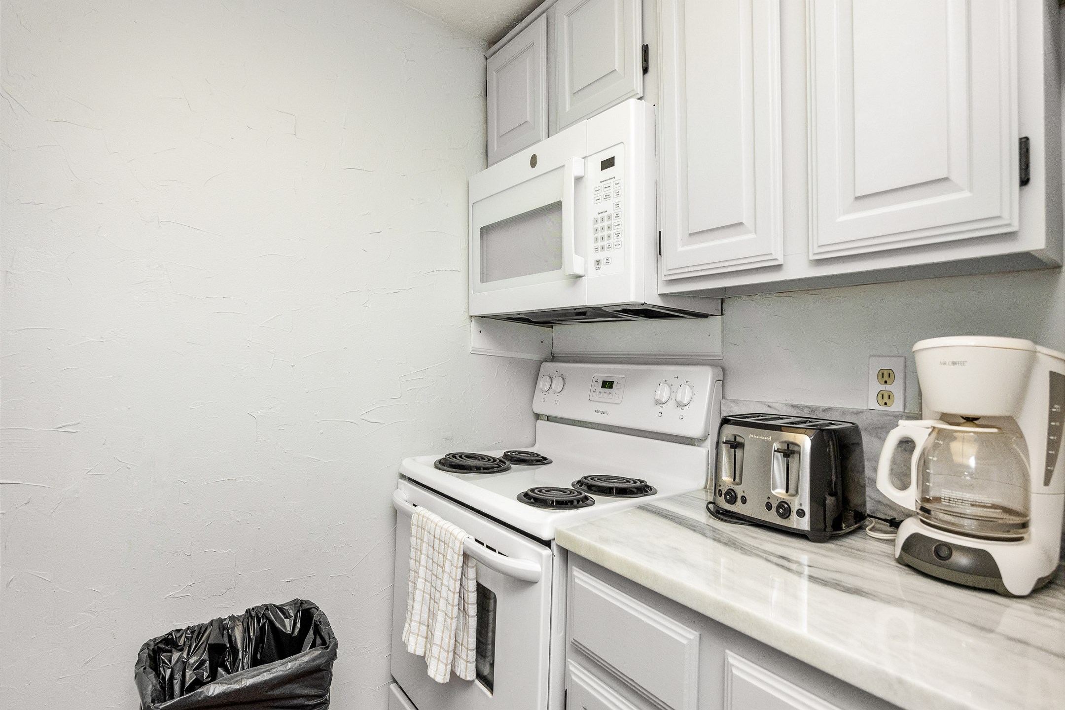 Fully equipped kitchen area with coffee maker, toaster, cookware, dinnerware, and other kitchen essentials provided