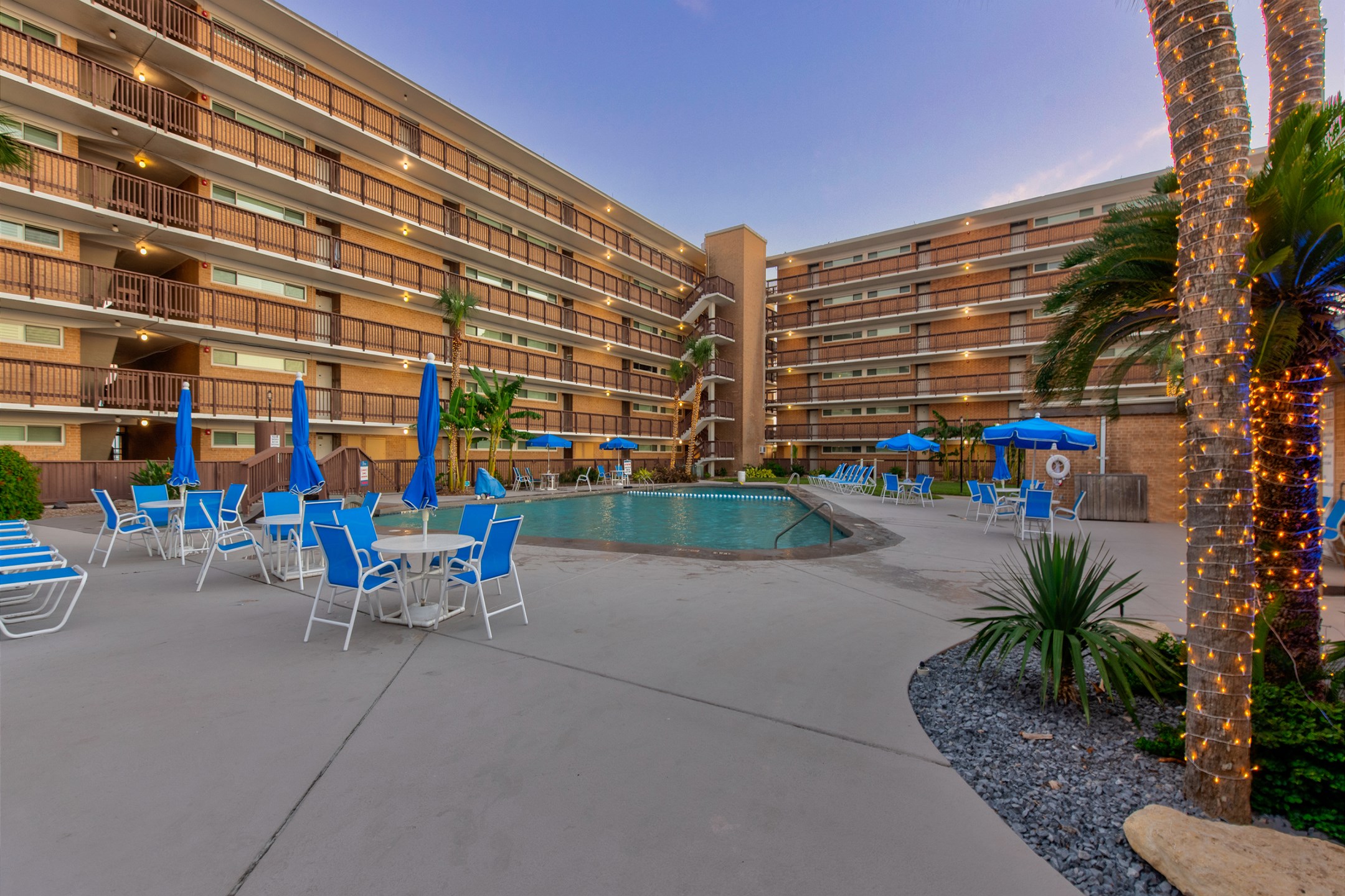 Inviting community pool with clear blue water, surrounded by comfy seating, beautiful palm trees and evening light