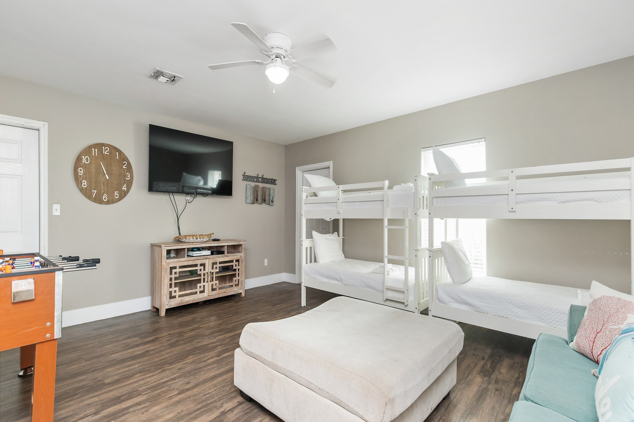 Multifunctional family room featuring two sets of twin bunk beds, a sleeper sofa, a television for entertainment, and a foosball table, making it ideal for both relaxation and play